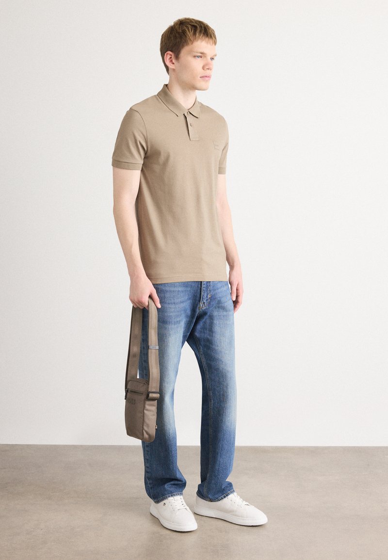 Polo beige, en tissu coton, design ajusté ; jeans bleus légèrement décolorés ; baskets blanches ; sac à bandoulière gris avec sangle.