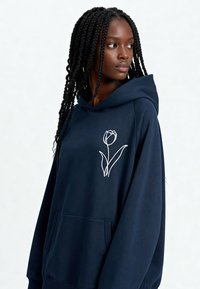 Sweat à capuche bleu marine avec un motif de tulipe brodé en blanc, fabriqué en tissu doux, avec une poche kangourou et des cordons de serrage réglables.