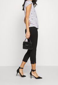 Svarta cropped jeans och en randig skjorta med marinblå ankare, kombinerat med svarta mocka stiletto-klackar och en liten svart handväska i konstl äder.