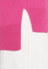 Fuchsiakvadratstickad tröja med ribbad mudd, slät textur, som visar en färgblockdesign mot vit textil.