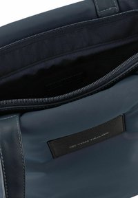 Sac fourre-tout bleu marine avec une finition lisse et brillante. Dispose d'une fermeture éclair et d'une patch texturé avec marque à l'intérieur de la partie supérieure.