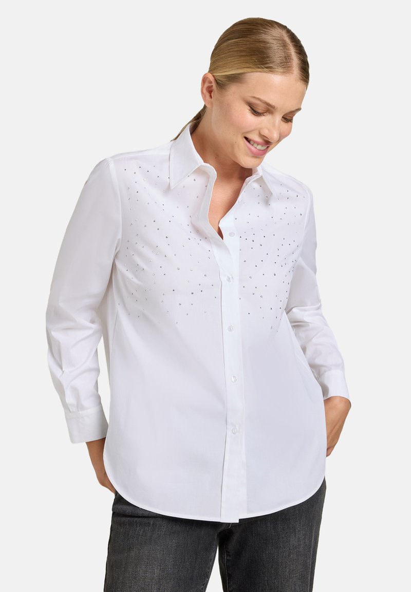 Camicia bianca con bottoni e maniche lunghe, caratterizzata da una sottile decorazione di piccoli dettagli scintillanti sulla parte anteriore. Tessuto dalla trama liscia.