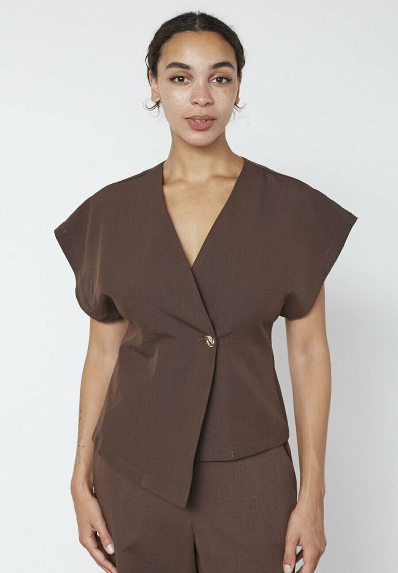 Brun kortærmet bluse med dyb V-udskæring og en enkelt guldknaplukning. Struktureret stof med løs pasform, parret med matchende bukser.