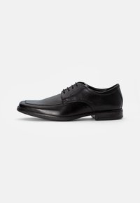 Chaussure habillée en cuir noir avec une finition lisse, bout rond, six œillets et un petit talon. Présente des détails de couture subtils et un look poli.