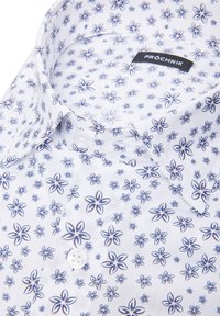 Biała koszula zapinana na guziki z granatowym kwiecistym wzorem, wykonana z bawełny, z kołnierzykiem w szpic i z przodem zapinanym na jeden biały guzik.