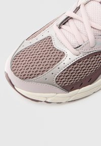 Ελαφρύ αθλητικό παπούτσι με άνω μέρος από δίχτυ σε αποχρώσεις του ροζ και καφέ, με ασημένιες λεπτομέρειες και υφασμένο πάτο για καλύτερη πρόσφυση.