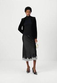 Black velvet blazer, black turtleneck, black satin skirt with lace trim, black high heels, and a small white handbag.