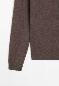 Bruine gebreide trui met lange mouwen, een zachte textuur en een geribde zoom. Het materiaal lijkt fijn met een consistent patroon.