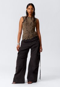 Olive-farbene Batik-Ärmelosen Top, kombiniert mit lockeren schwarzen Cargo-Hosen. Die Hosen verfügen über große Taschen und dekorative Nähte.