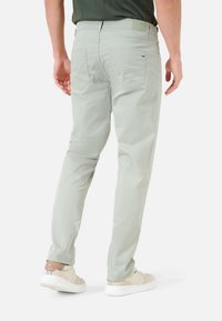 Lichtgroene broek met een slim fit, gemaakt van zachte stof, met twee achterzakken en een gladde tailleband, gecombineerd met beige sneakers.