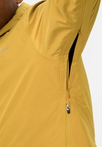 Geel waterdichte jas met een gladde textuur, een ritssluiting zijzak en versterkte stiksels. Voorzien van reflecterende branding op de borst.