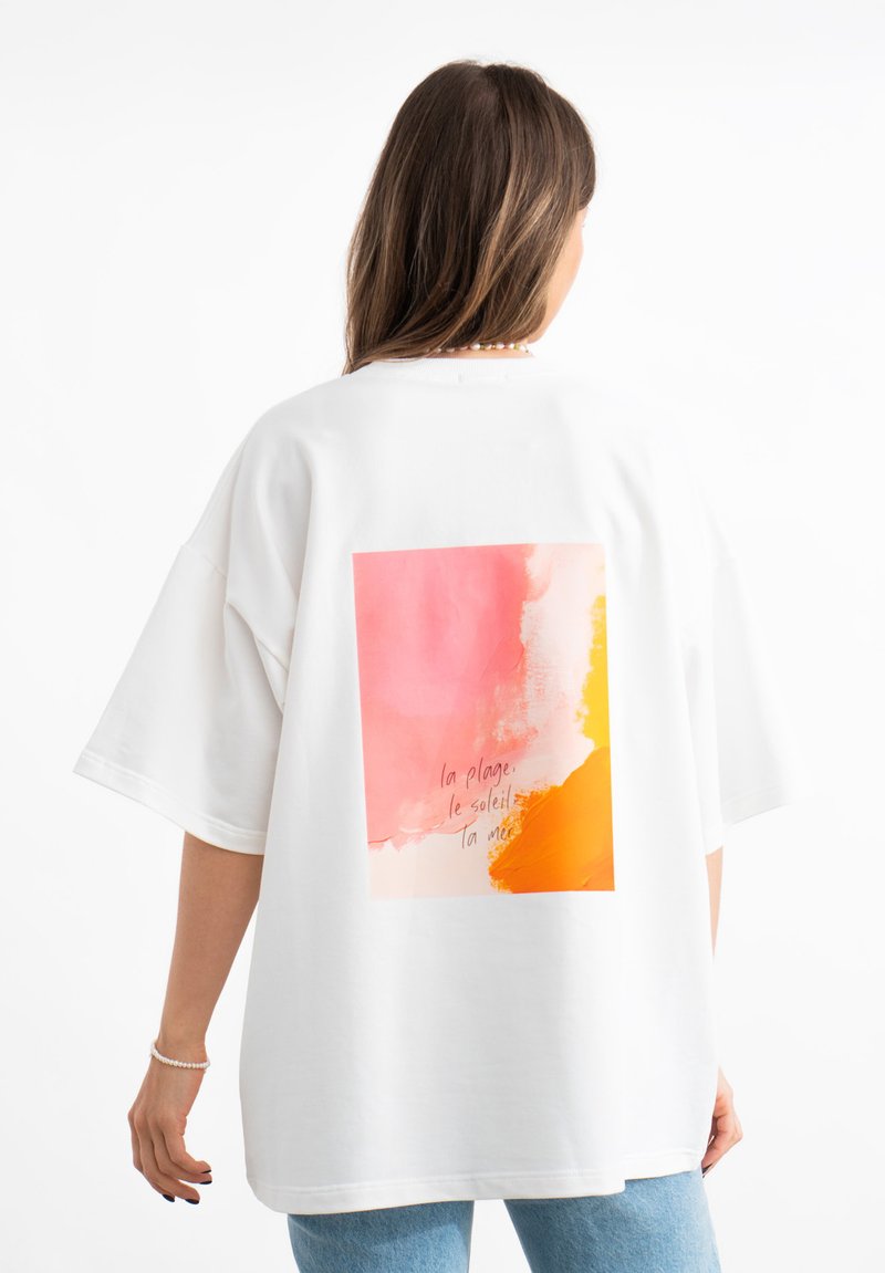 Witte oversized t-shirt met een kleurrijk abstract ontwerp op de achterkant in roze, oranje en gele tinten, met daarop bedrukte tekst.