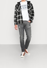 Černo-bílá kostkovaná flanelová košile, bílý tričko s logem "Scotch & Soda", šedé roztrhané džíny a vícebarevné vysoké tenisky.