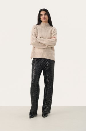 Maglione beige a trecce con colletto alto, abbinato a pantaloni larghi neri con paillettes e scarpe nere con punta.