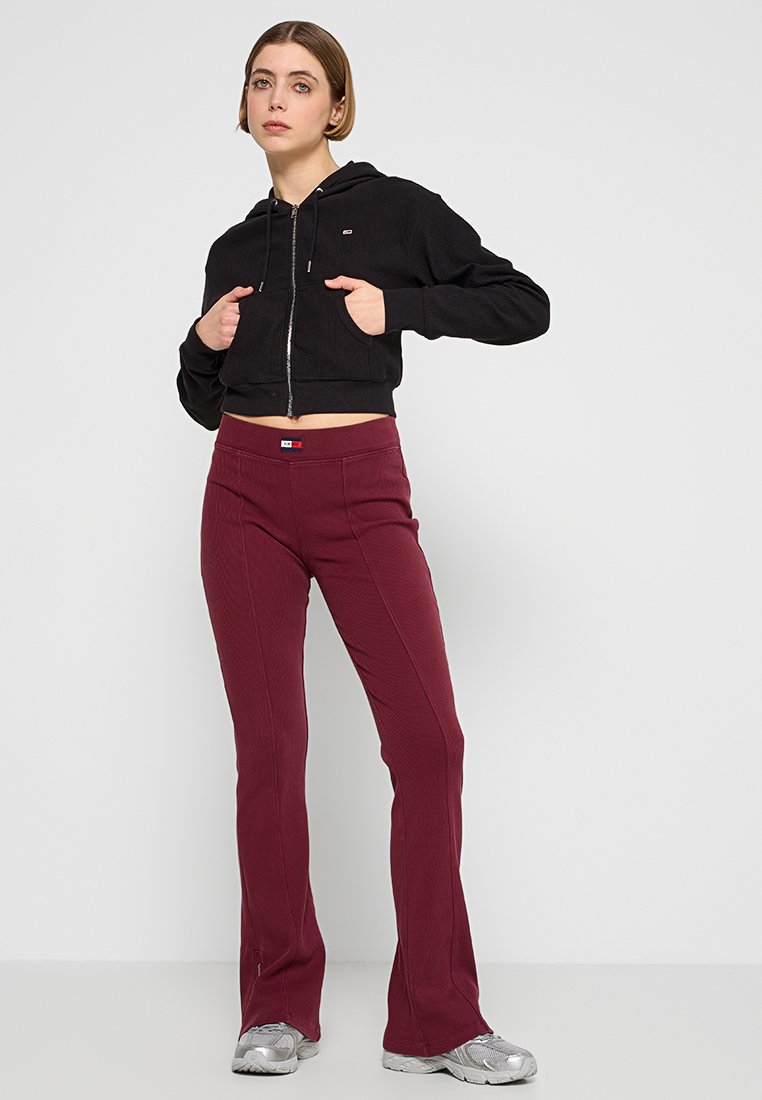 Zwarte cropped hoodie met een rits, geribbelde textuur en kangoeroe pockets, gecombineerd met bordeauxrode flared pants met stiksels en een logo.