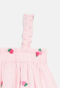 Bretelle de robe en tissu rose texturé avec détails froncés et fraises rouges brodées avec feuilles vertes.