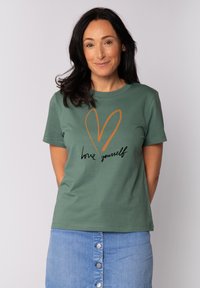 T-shirt en coton vert avec un design de cœur orange et le texte "aime-toi" en noir. Manches courtes et col rond.