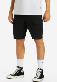 Sorte cargo shorts med flere lommer, en afslappet pasform og slidstærkt stof. Sammen med hvide sokker og sorte høj-top sneakers.