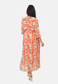 Maxikjole i levende orange med blomsterdesign, der har trekvartærmer og en indsnævret talje. Let og gennemsigtig tekstur.