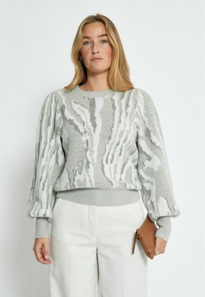 Maglione grigio chiaro con motivi astratti bianchi, collo rotondo e maniche a sbuffo. Orlo e polsini a coste. Tessuto liscio, abbinato a pantaloni crema.