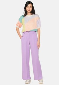Multicolored knit sweater with geometric patterns and short sleeves, paired with high-waisted, wide-leg lavender trousers and white sneakers.
