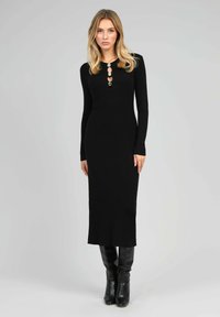 Robe noire à manches longues en côtes avec des détails de boutons au niveau du col et une silhouette droite, associée à des bottes noires montantes.