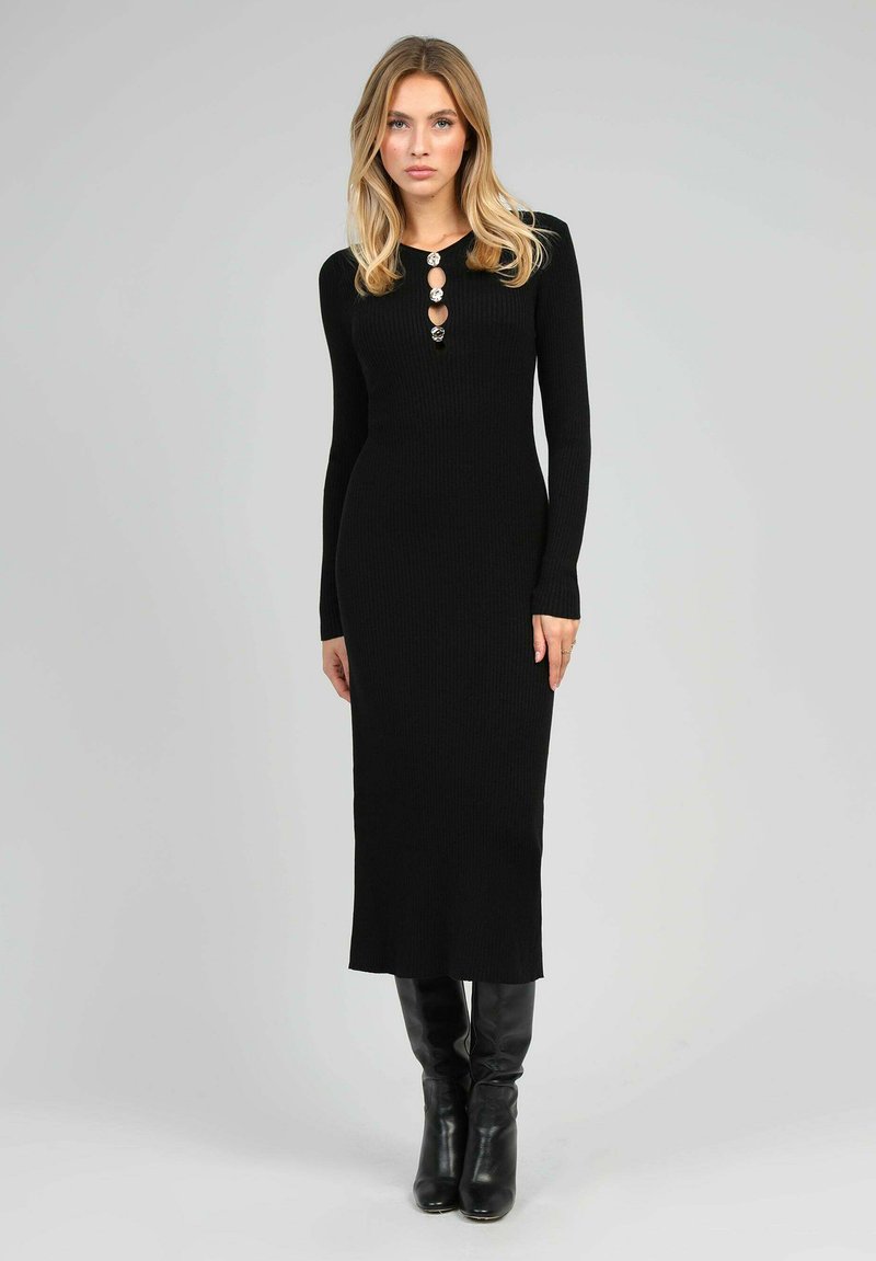 Robe noire à manches longues en côtes avec des détails de boutons au niveau du col et une silhouette droite, associée à des bottes noires montantes.