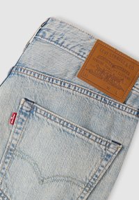 Világoskék farmernadrág, visszahajtva, hogy látható legyen a hátsó zseb, rajta a Levi's piros címkével és a barna bőr Levi Strauss & Co. címkével.