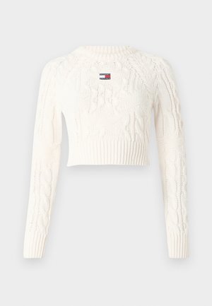 Cremfarbener Kabelstrickpullover mit langen Ärmeln, rundem Halsausschnitt und cropped Design. Mit einem kleinen Logo-Patch auf der Vorderseite.