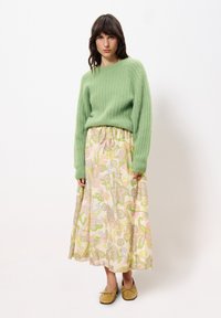 Grüner gerippter Strickpullover, maximaler Rock mit floralen Mustern in Pastellfarben und goldenen flachen Schuhen mit Schleifen. Lässige Passform und weiche Texturen.
