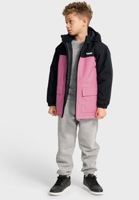 Veste à capuche noire et rose avec poches avant, assortie à un pantalon de sport gris et des baskets noires. Comprend des poignets élastiques et une fermeture éclair.