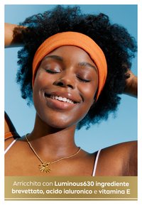 Giovane con capelli neri ricci, che indossa un cerchietto arancione e una collana d'oro con un ciondolo a forma di sole, su uno sfondo blu.