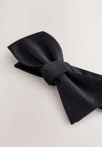 Black textured bow tie with a woven pattern, featuring a central knot and pointed ends. Flat layout against a neutral background.