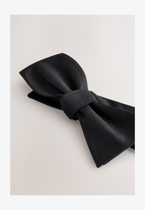 Schwarze, strukturierte Fliege mit gewebtem Muster, zentraler Knoten und spitzen Enden. Flach liegend auf neutralem Hintergrund.