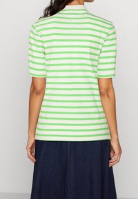 Striped green and white short-sleeve polo shirt with a collar, smooth texture, and a relaxed fit, paired with a dark denim skirt.