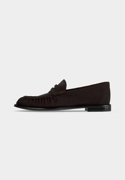 Mocassin en cuir marron foncé avec un petit talon, couture mocassin et un détail de bride sur le dessus, sur un fond uni.