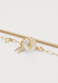 Gold jewelry piece with a pearl and eye design, featuring crystal accents, a textured chain, and a sleek, polished finish.