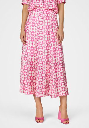 Woman wearing a pink and white geometric patterned midi skirt with an elastic waistband and pink open-toe block heel sandals.