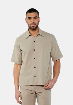 Camicia a maniche corte di un leggero colore beige, con tessuto testurizzato, orlo dritto, bottoni neri e colletto classico.