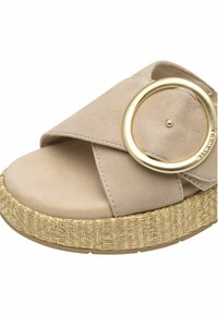Sandale plateforme en suède beige avec un design à brides croisées, ornée d'un grand accent circulaire doré et d'une semelle extérieure texturée tissée.