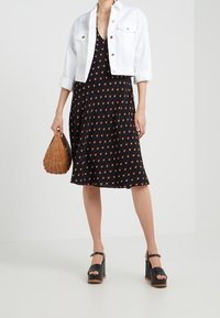 Vestido negro con un patrón floral, chaqueta de mezclilla blanca cortada, bolso de mimbre y zapatos de plataforma negros con diseño de punta descubierta.