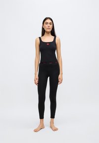 Débardeur noir à encolure carrée avec détail logo, associé à un legging noir doté d'une ceinture avec accents rouges. Tissu lisse, coupe ajustée.