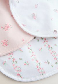 Három pamut előke: egy rózsaszín virágmintával, egy fehér tündér- és virágmintákkal, valamint egy fehér, függőleges virágdíszítésekkel.