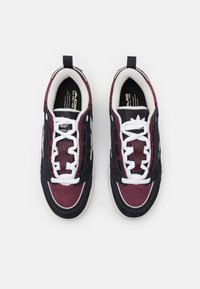 Para czarnych i ciemnoczerwonych sneakersów z białymi sznurowadłami i wewnętrzną wyściółką, widzianych z góry na białym tle.