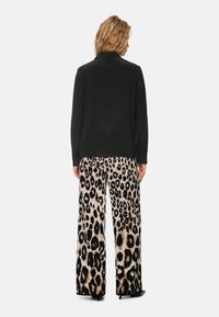 Schwarzes Langarmshirt kombiniert mit weit geschnittenen Hosen, die ein beiges und schwarzes Leopardenmuster aufweisen, mit glatter Stoffstruktur und entspanntem Schnitt.