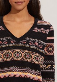 Sweter dzianinowy o czarnym tle z kolorowymi kwiatowymi i geometrycznymi wzorami. Projekt wycięcia w serek z fakturowanymi detalami i poziomymi paskami.