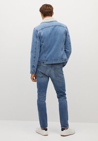 Chaqueta de mezclilla azul claro con un cuello de borrego, combinada con jeans a juego. El diseño presenta un estilo ajustado y cinco bolsillos.