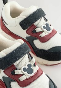 Dziecięce sneakersy z białą siateczkową bazą, bordowymi i czarnymi akcentami, rzepem oraz szarym emblematem Myszki Miki na sznurówkach.
