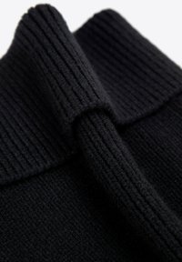 Tessuto di maglione nero a coste con una texture morbida, che mostra un colletto piegato e una finitura liscia. Attenzione al motivo fitto e al materiale.