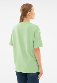 Jasnozielona bawełniana koszulka o luźnym fasonie, z krótkimi rękawami i okrągłym dekoltem, prezentowana od tyłu. Prosty i pozbawiony ozdób design.